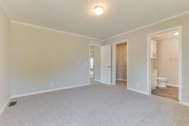 unfurnished bedroom with crown molding, ensuite bath, light carpet, a closet, and a spacious closet