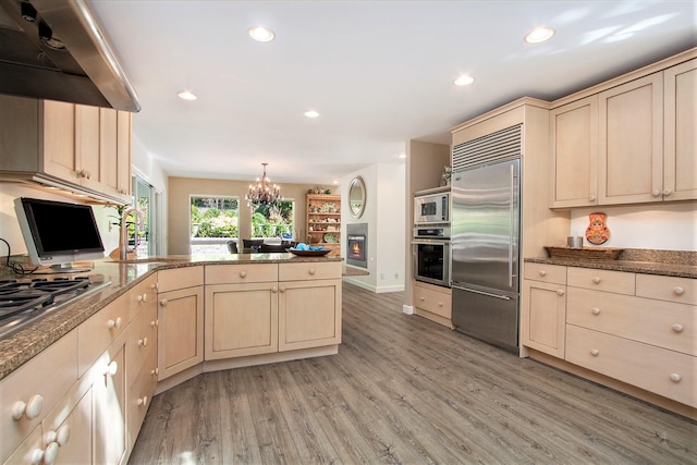 kitchen featuring built in appliances, a notable chandelier, range hood, light hardwood / wood-style floors, and kitchen peninsula