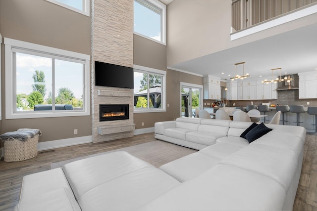 living room featuring light wood-type flooring, a high ceiling, a notable chandelier, and a stone fireplace