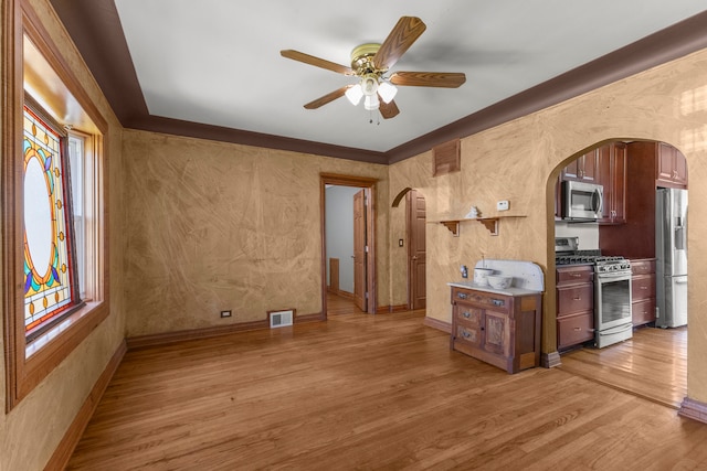 kitchen with light wood-type flooring, appliances with stainless steel finishes, ornamental molding, and ceiling fan