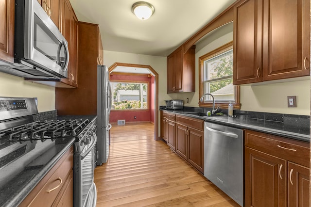 kitchen with dark stone counters, light hardwood / wood-style flooring, stainless steel appliances, and sink