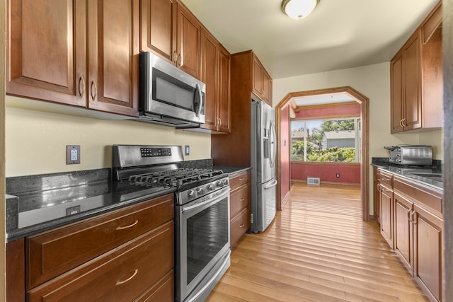 kitchen featuring dark stone countertops, light wood-type flooring, and appliances with stainless steel finishes