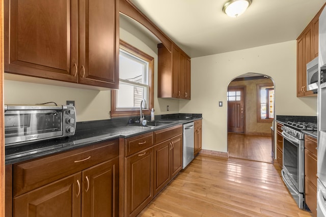 kitchen featuring light wood-type flooring, sink, appliances with stainless steel finishes, and dark stone counters