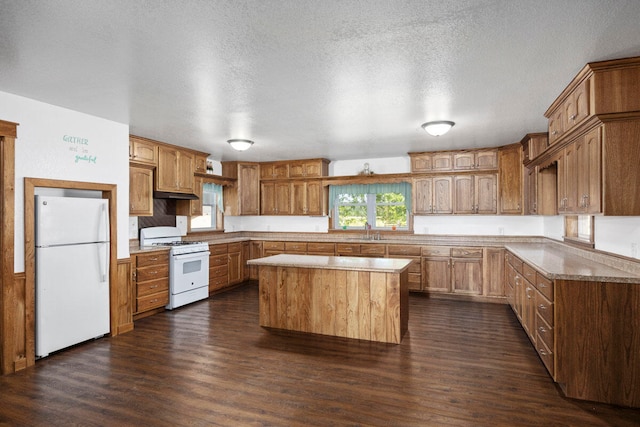 kitchen featuring dark wood-type flooring, white appliances, a center island, and a textured ceiling