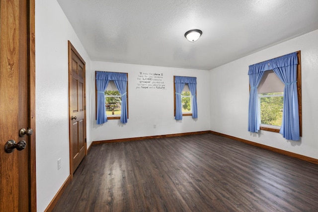 empty room with a textured ceiling, a healthy amount of sunlight, and dark hardwood / wood-style floors