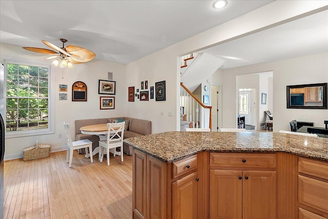 kitchen with ceiling fan, light wood-type flooring, and stone counters