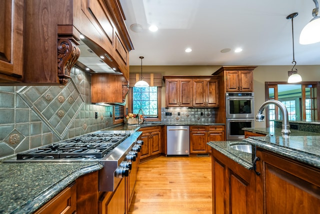 kitchen featuring pendant lighting, appliances with stainless steel finishes, tasteful backsplash, light hardwood / wood-style floors, and dark stone counters