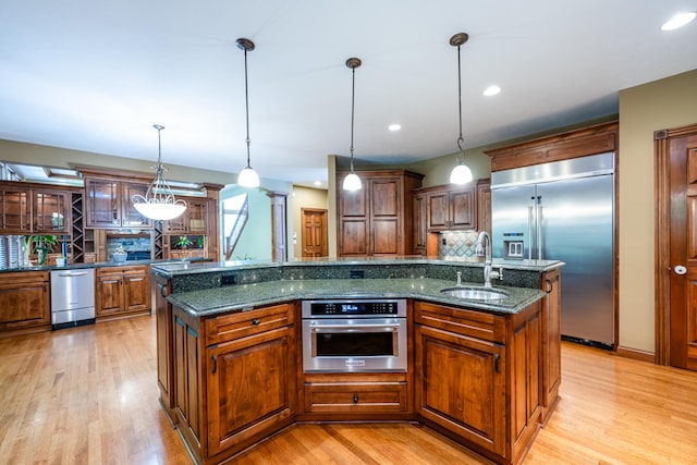 kitchen featuring decorative light fixtures, appliances with stainless steel finishes, and a kitchen island with sink