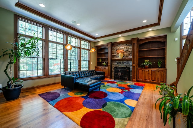 living room featuring a fireplace, crown molding, wood-type flooring, and a tray ceiling