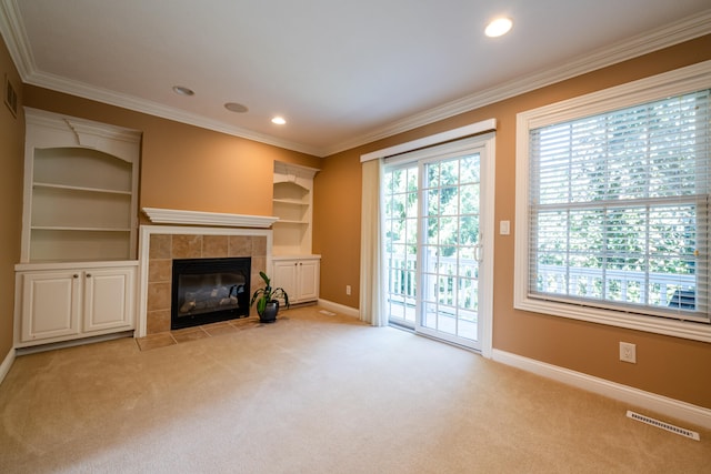 unfurnished living room featuring crown molding, built in shelves, light colored carpet, and a tile fireplace