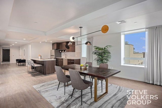 dining area featuring light wood-type flooring, a raised ceiling, and sink