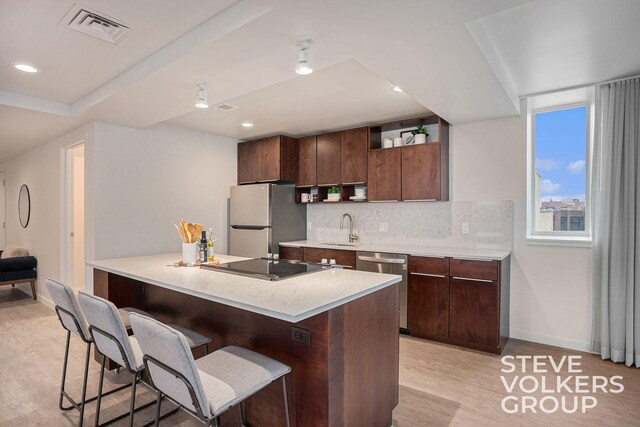 kitchen with light hardwood / wood-style flooring, appliances with stainless steel finishes, sink, a breakfast bar area, and dark brown cabinetry