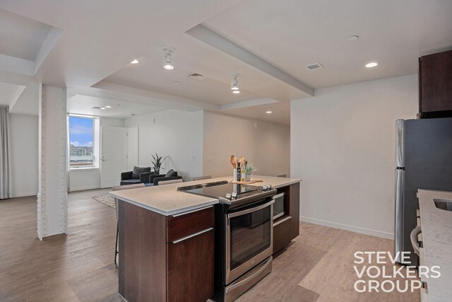 kitchen with appliances with stainless steel finishes, a center island, light hardwood / wood-style floors, and dark brown cabinets