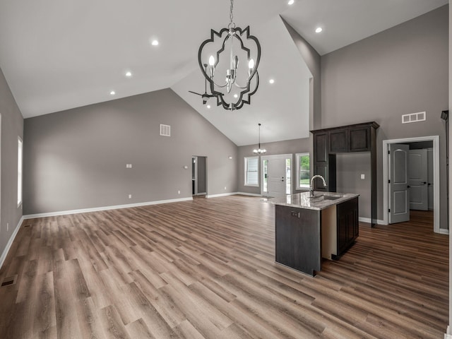 kitchen featuring dark brown cabinets, high vaulted ceiling, hardwood / wood-style flooring, a chandelier, and light stone counters