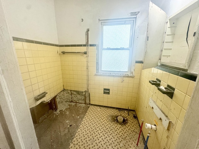 full bath featuring a tile shower, a wainscoted wall, and tile walls