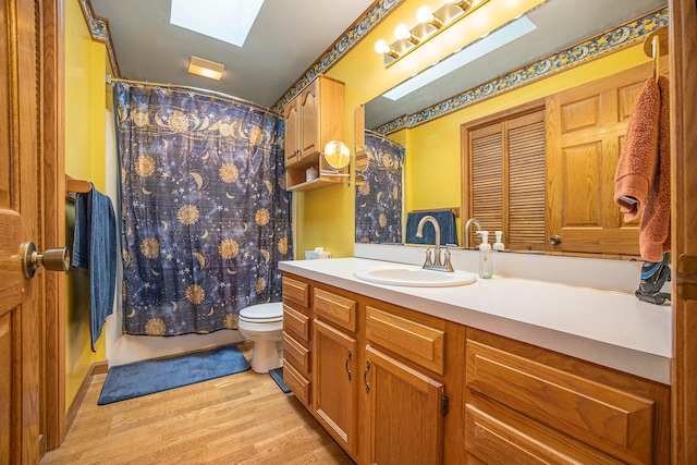 bathroom with toilet, vanity, hardwood / wood-style flooring, a skylight, and a shower with shower curtain