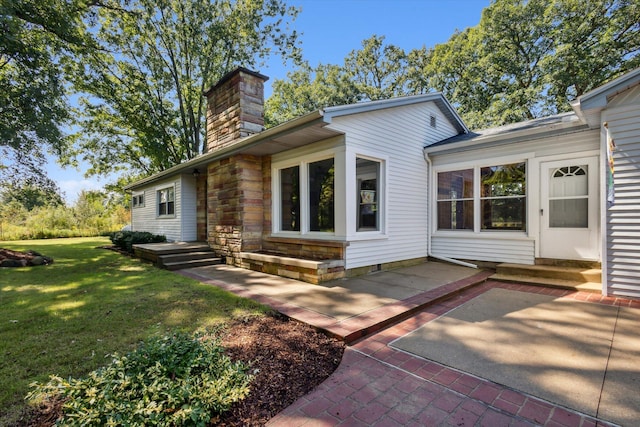 back of property with a yard, stone siding, a chimney, and a patio area