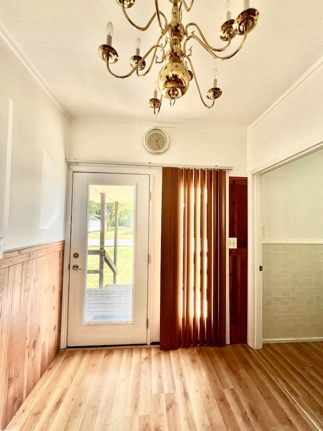 doorway to outside featuring light wood-type flooring, crown molding, and a chandelier