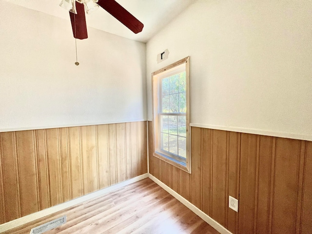 empty room featuring wood walls, ceiling fan, and light hardwood / wood-style floors