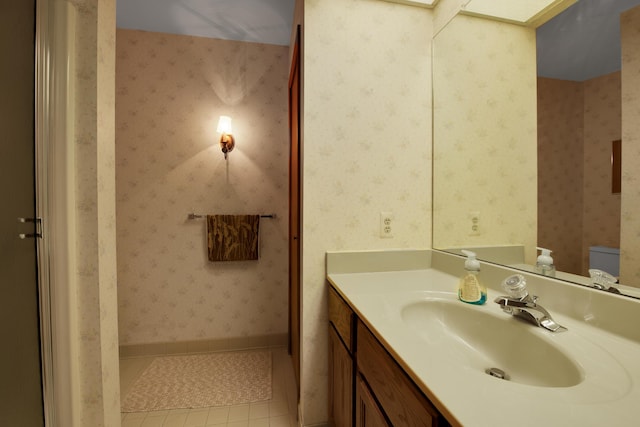 bathroom with tile patterned floors, toilet, wallpapered walls, baseboards, and vanity