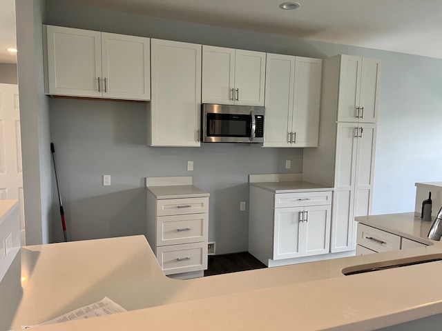 kitchen featuring a sink, stainless steel microwave, light countertops, and white cabinetry