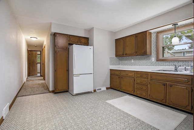 kitchen with a sink, tasteful backsplash, light countertops, and freestanding refrigerator