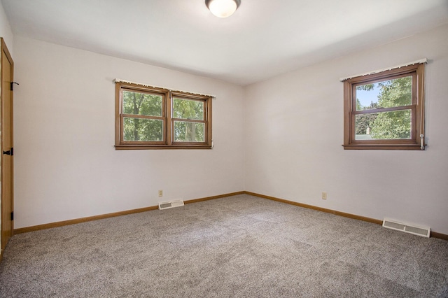 carpeted spare room with a healthy amount of sunlight, visible vents, and baseboards