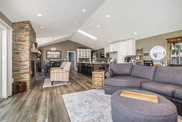 living room featuring vaulted ceiling, dark hardwood / wood-style floors, a stone fireplace, and a notable chandelier