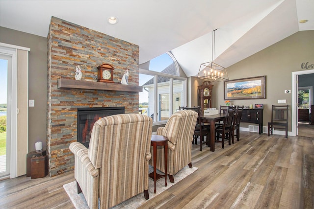 dining room with hardwood / wood-style floors, a wealth of natural light, a notable chandelier, and a stone fireplace