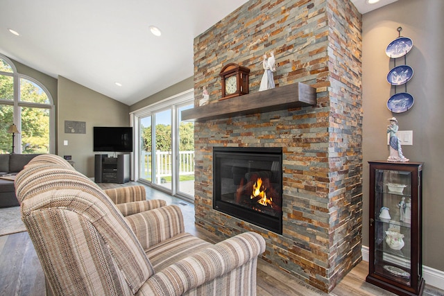 living room with vaulted ceiling, a wealth of natural light, hardwood / wood-style floors, and a stone fireplace