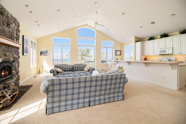 living room featuring lofted ceiling, ceiling fan, light carpet, and a stone fireplace