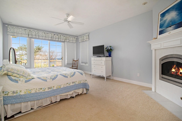 bedroom featuring light colored carpet, ceiling fan, a tiled fireplace, and access to outside