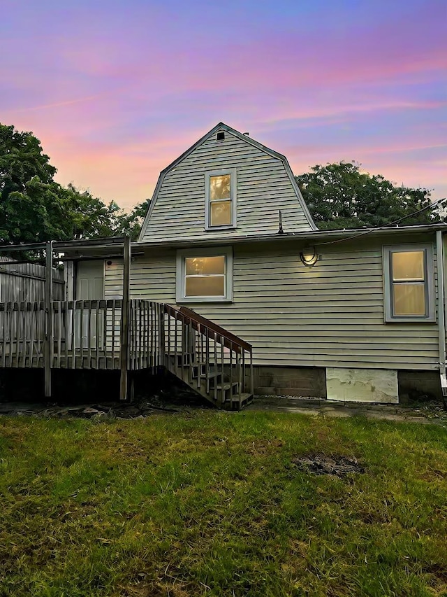 back of house at dusk with a gambrel roof, a wooden deck, and a yard