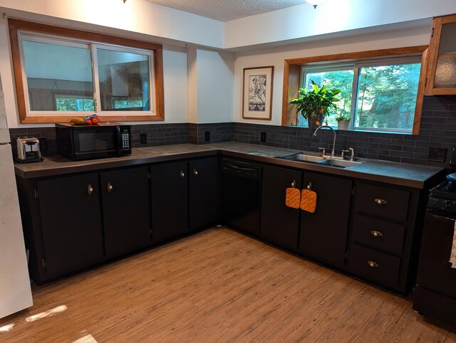 kitchen with a textured ceiling, light hardwood / wood-style flooring, backsplash, black appliances, and sink