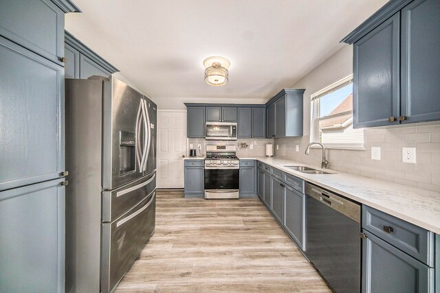 kitchen featuring light stone counters, sink, tasteful backsplash, appliances with stainless steel finishes, and light hardwood / wood-style floors