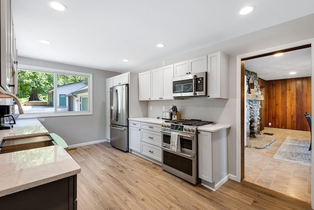 kitchen with wood walls, stainless steel appliances, light stone counters, light wood-type flooring, and white cabinets