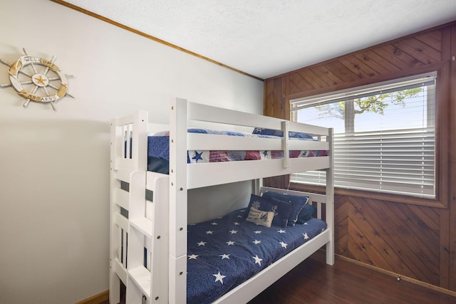 bedroom with a textured ceiling, wood walls, and dark hardwood / wood-style floors