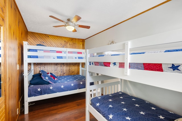 bedroom featuring a textured ceiling, wood walls, dark hardwood / wood-style flooring, ornamental molding, and ceiling fan