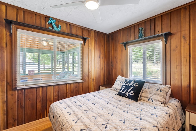 bedroom featuring a textured ceiling, ceiling fan, and wooden walls