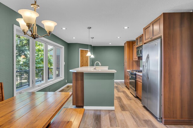 kitchen featuring appliances with stainless steel finishes, a kitchen island with sink, light hardwood / wood-style flooring, a chandelier, and hanging light fixtures