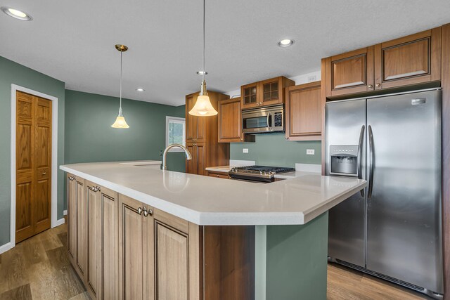 kitchen with appliances with stainless steel finishes, decorative light fixtures, light hardwood / wood-style floors, and an island with sink