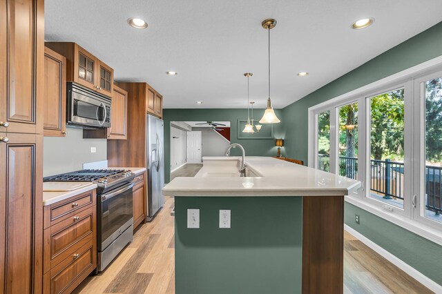 kitchen with appliances with stainless steel finishes, a kitchen island with sink, ceiling fan, sink, and decorative light fixtures