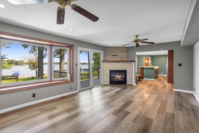 unfurnished living room with ceiling fan, a fireplace, a water view, and hardwood / wood-style flooring