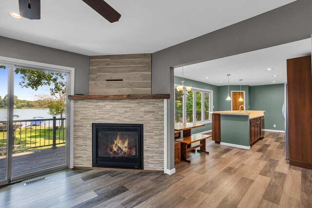 living room with hardwood / wood-style floors, ceiling fan with notable chandelier, a water view, sink, and a tiled fireplace