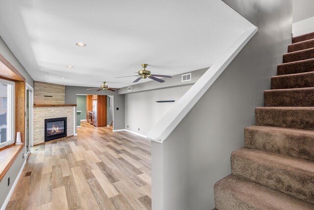 unfurnished living room with light hardwood / wood-style flooring, ceiling fan, and a tiled fireplace