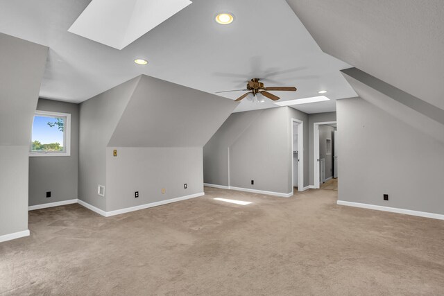 additional living space with vaulted ceiling with skylight, ceiling fan, and light colored carpet