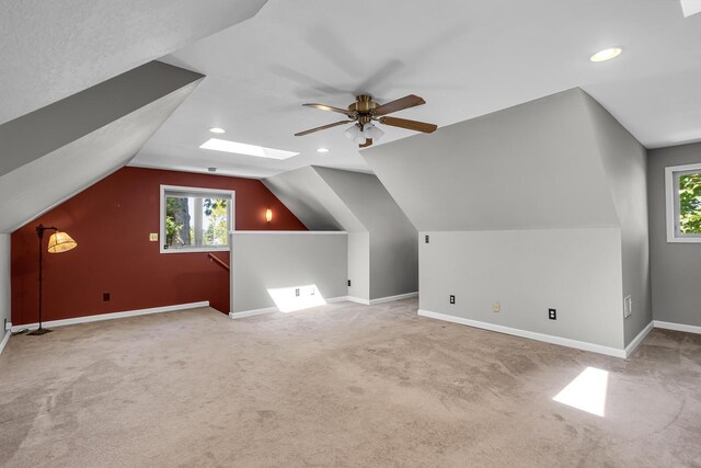 additional living space featuring light carpet, ceiling fan, and vaulted ceiling with skylight