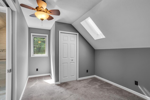 bonus room featuring ceiling fan, vaulted ceiling with skylight, and light carpet