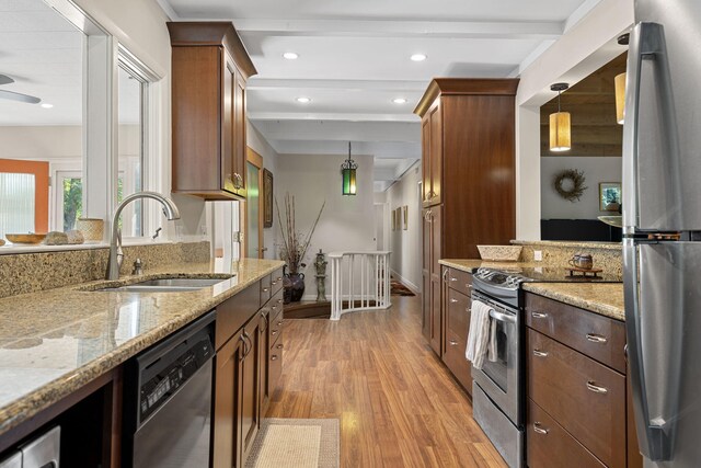 kitchen with appliances with stainless steel finishes, hanging light fixtures, light stone counters, light hardwood / wood-style flooring, and sink