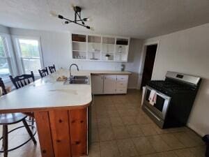 kitchen featuring a chandelier, a kitchen breakfast bar, sink, stainless steel stove, and white cabinets